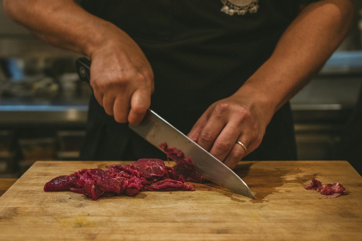 Cuisinier tranchant une viande crue au couteau sur une planche en bois