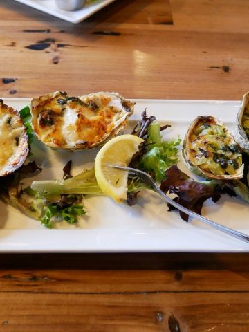 Six huîtres gratinées au four dans leur coquille, garniture au fromage et aux épinards, servies sur une assiette