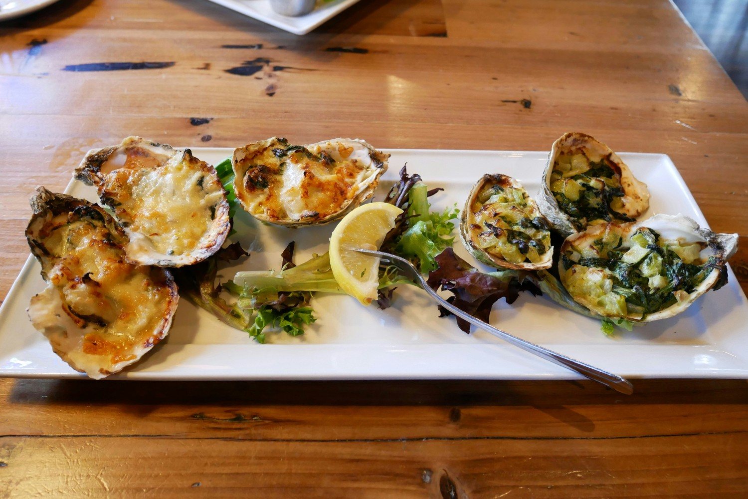 Six huîtres gratinées au four dans leur coquille, garniture au fromage et aux épinards, servies sur une assiette