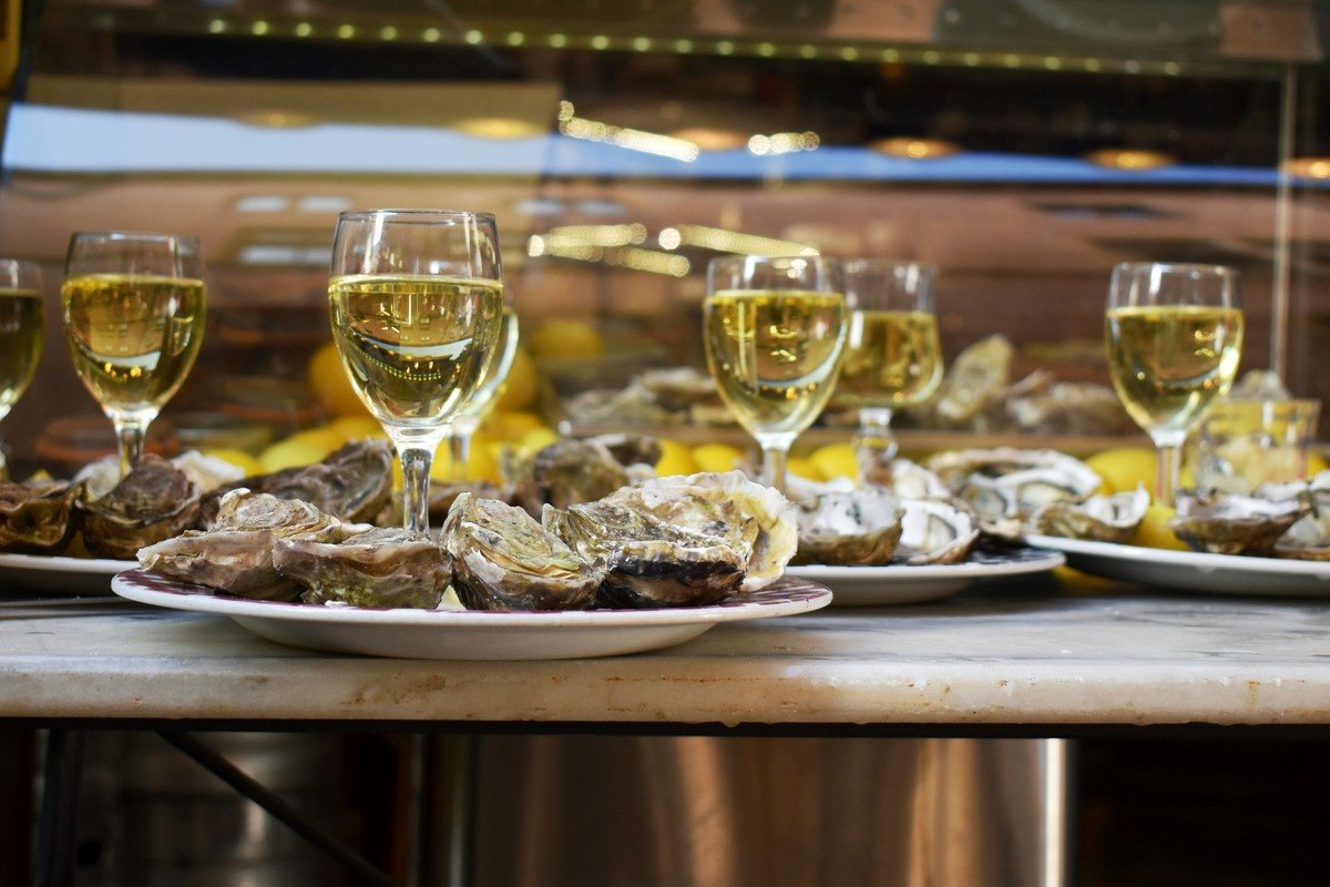 Assiettes d'huîtres et verres de vin blanc alignés sur le comptoir d'un café à Lyon
