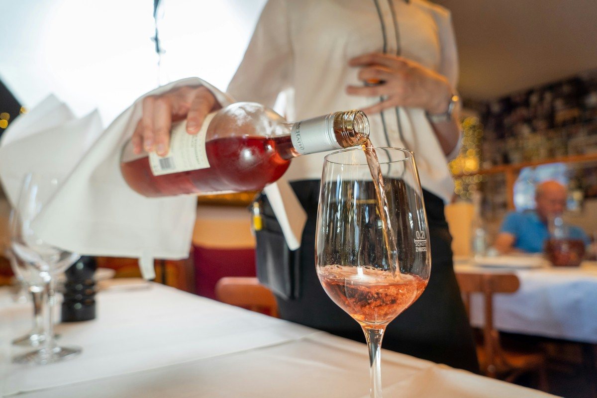 Serveur en salle versant un vin rosé dans un verre, bouteille tenue avec une serviette blanche