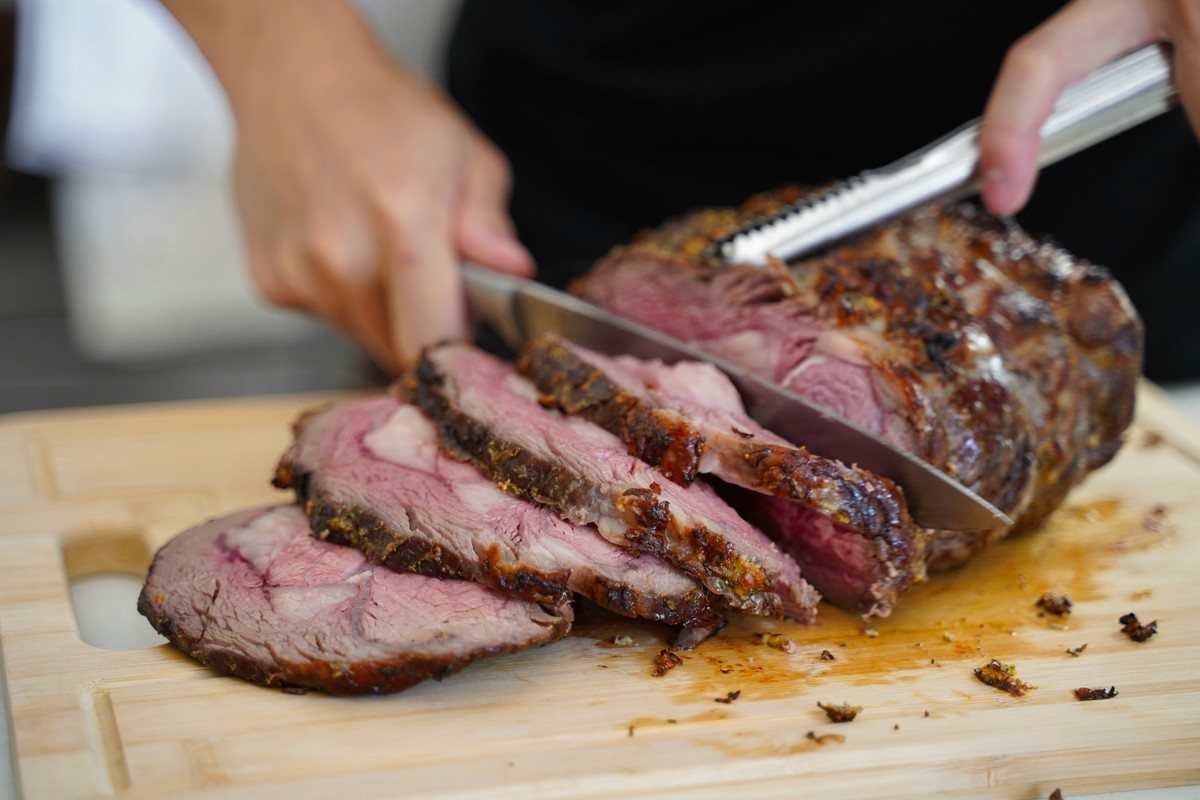 Découpe d'un rôti de bœuf en tranches régulières avec une lame longue sur une planche en bois