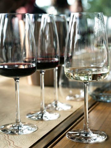 Trois verres de vin alignés sur une table, deux rouges et un blanc, prêts pour un service en séquence