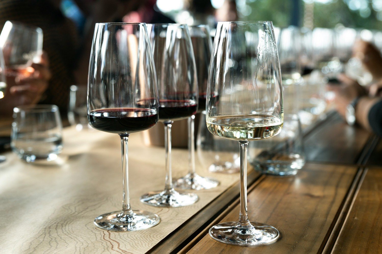 Trois verres de vin alignés sur une table, deux rouges et un blanc, prêts pour un service en séquence